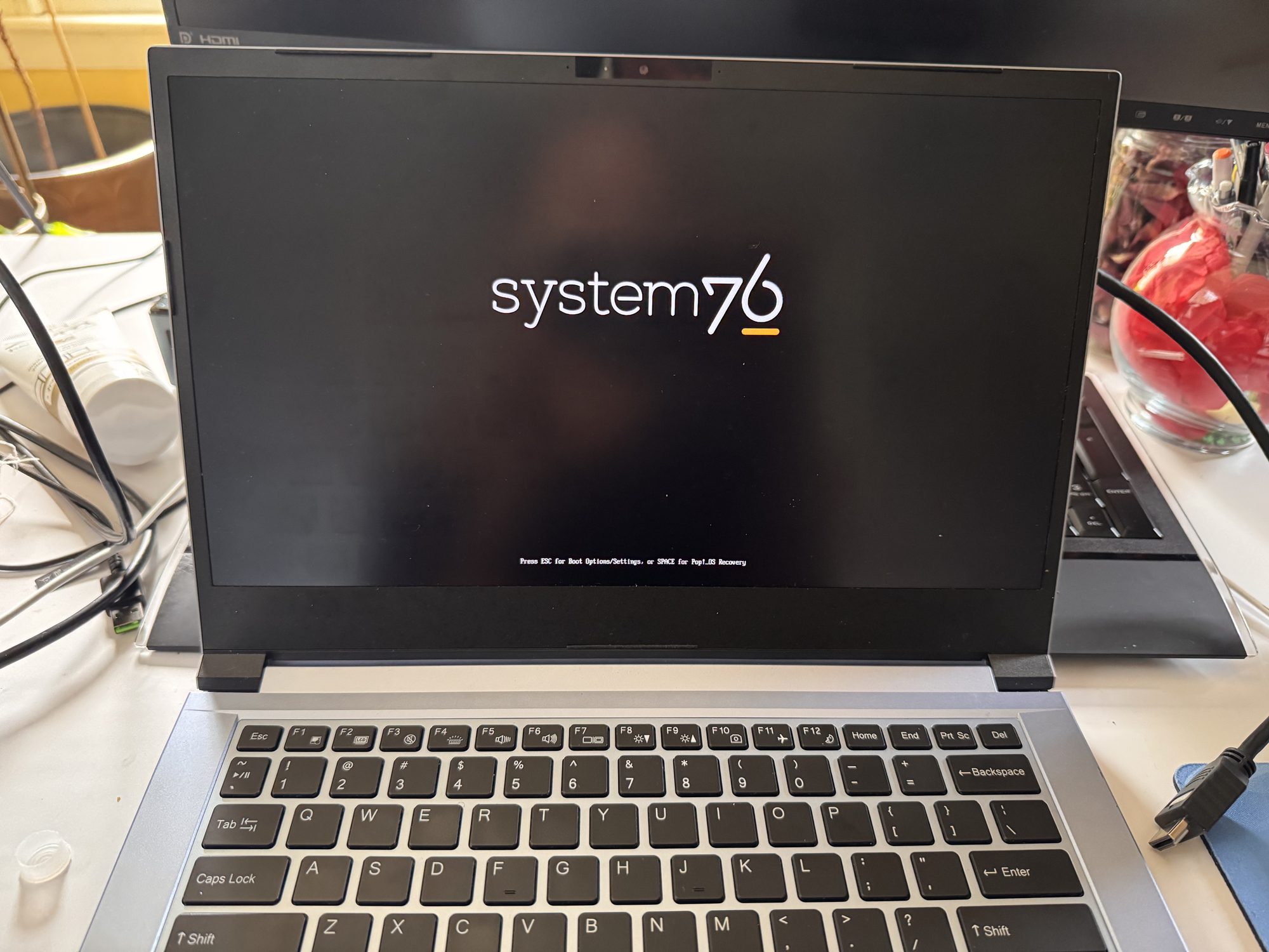 Galago Pro 6 laptop screen lit up and showing the System76 boot logo, reflecting a person standing in front of it.
